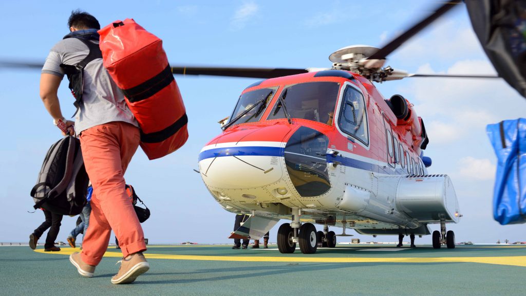 passenger carry his baggage to embark helicopter at oil rig plat